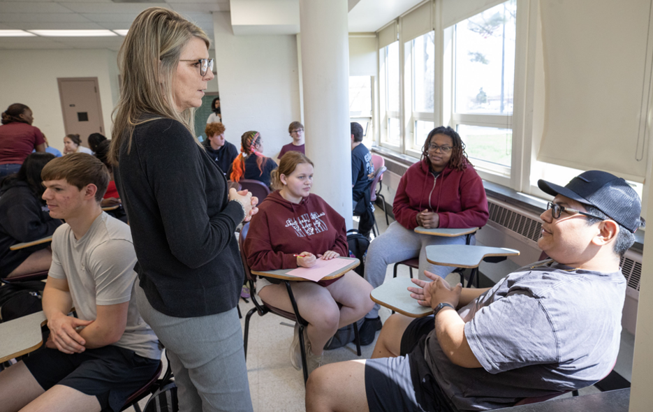 Teacher speaking with a group of students in a classroom setting.
