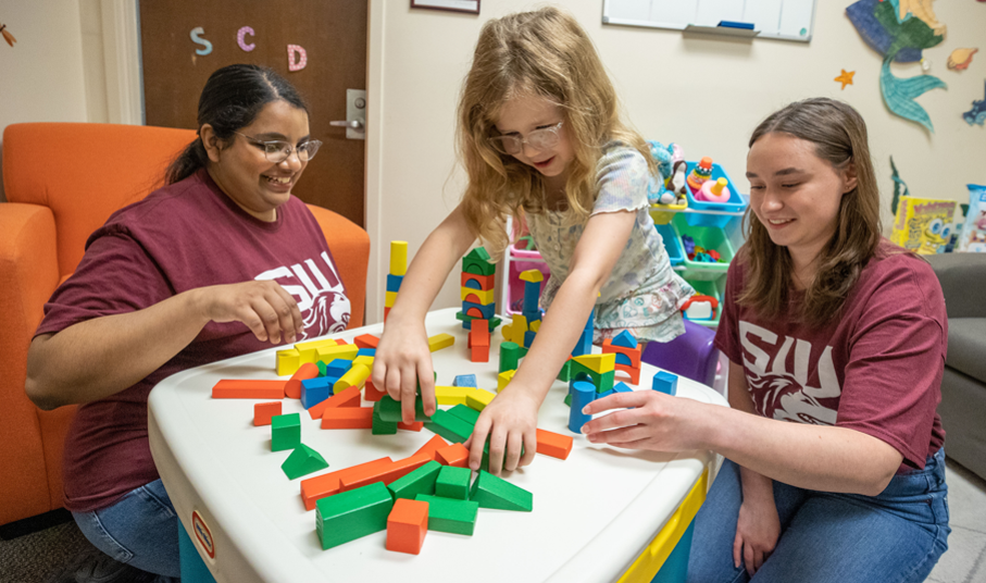 Two teachers help a student to assemble a puzzle.